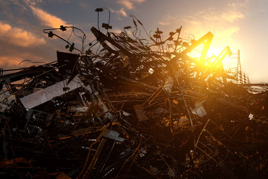 A large pile of rusty scrap metal in a landfill outside the city. Against the background of the sunset sky.
