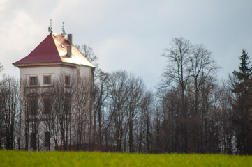 a white tower with a red roof on a hill behind a field and trees