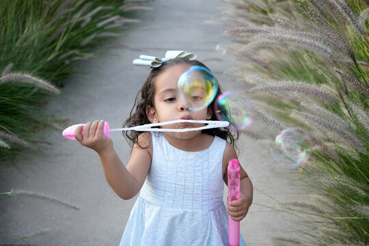 Ni&ntilde;a hermosa latina al aire libre en el parque disfrutando jugando haciendo soplando burbujas sonriendo en un hermoso atardecer al aire libre sorprendida