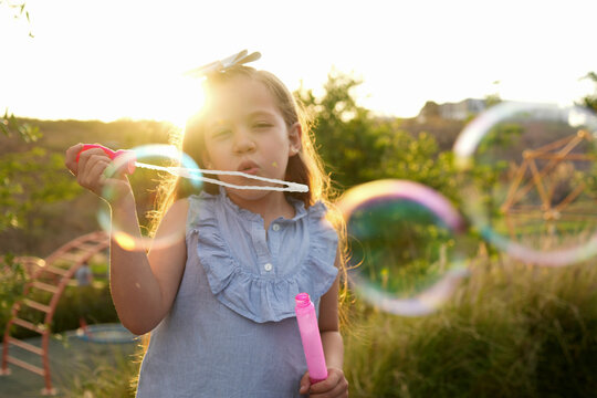 Ni&ntilde;a hermosa latina al aire libre en el parque disfrutando jugando haciendo soplando burbujas sonriendo en un hermoso atardecer al aire libre sorprendida