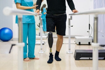Physiotherapist helping patient with prosthetic leg at parallel bars