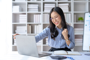 Happy asian businesswoman raising hands with victory smiling happily on laptop computer. The concept of success at work.