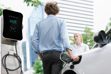 Progressive businessman and businesswoman with electric car parking and connected to public...
