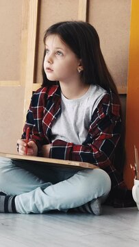 Vertical video. Art hobby. Kids painting. Artistic tools. Girl drawing with colorful pencils sitting floor in light room interior.