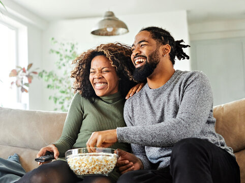 television watching couple tv home woman man remote movie entertainment sofa lifestyle sitting fun popcorn happy young smiling female happiness love leisure together