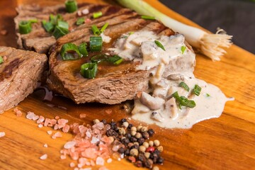 Rump steak on a wooden board with mushroom sauce. Quality beef. Barbecue season. Medium grilled steak.