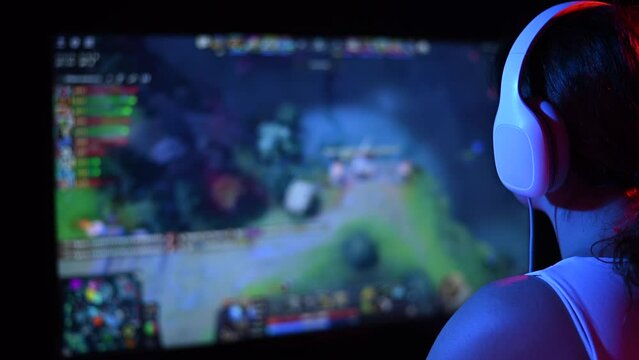 Rear view of a caucasian woman playing a computer game in neon light in the dark.