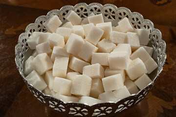Sugar cubes in a metal bowl on the table. Natural refined pressed sugar close-up