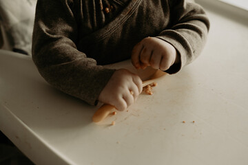 6 months old baby playing with spoon after eating baby food. Close up of baby hands and spoon with vegetable puree.