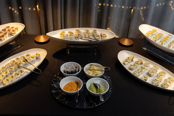 platters of different sushi rolls and small bowls of ginger soy sauce wasabi and spicy mayo in the center