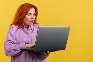 Naklejka premium Redheaded mature woman with a surprised look using a laptop
