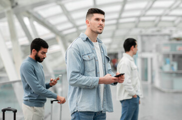 Male Traveler Using Mobile Phone Standing With Passengers In Airport