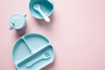 Silicone bib, plate, cup, cutlery on pink background. Serving baby food concept. Flat lay, top view.