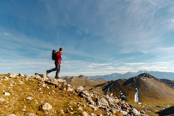 white male mountaineer with red clothes and backpack ascending a mountain peak during a hiking...