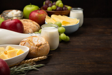 Jewish Shavuot Holiday Card. Dairy Products, Fruits, Cheese, Bread, Milk on Brown Wooden Background.