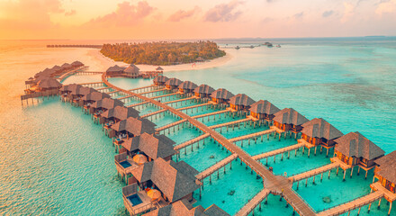 Fototapeta premium Aerial sunset panoramic landscape luxury tropical resort water villas. Beautiful island beach orange sunrise sea sky. Amazing bird eyes panorama Maldives paradise tropical bay. Exotic summer vacation