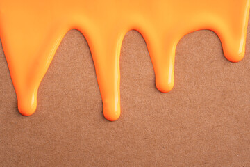 Orange liquid drops of paint color flow down on craft paper. Abstract art. Orange paint dripping on brown recycled paper