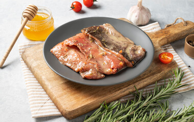 Raw salmon, greased with honey marinade with spices on a plate on a light background with fresh herbs and vegetables.