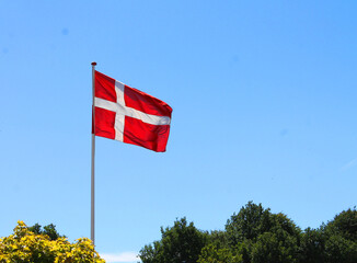 Red and white Danish flag in the blue sky on a sunny celebrations day in Denmark