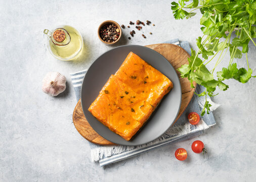 Raw salmon, greased with marinade with spices on a plate on a light background with fresh herbs and vegetables. Healthy dietary homemade food.
