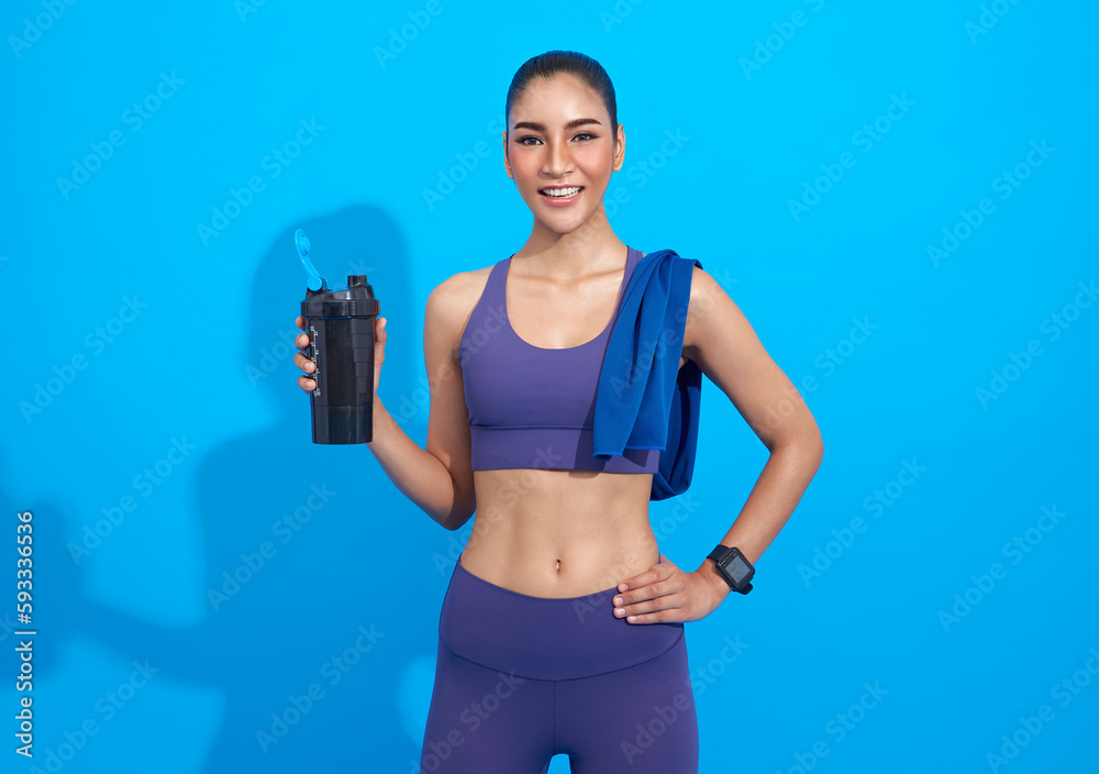 Wall mural beautiful smiling asian sporty woman in purple sportswear and towel on neck holding shaker with heal