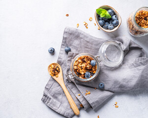 Homemade baked granola with nuts and fresh blueberry in a jar on a light background with napkin. Healthy vegetarian muesli for breakfast.