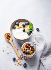 Homemade baked granola with yogurt, blueberries and banana in a bowl on a light background with fresh berries. Healthy vegetarian breakfast with muesli.