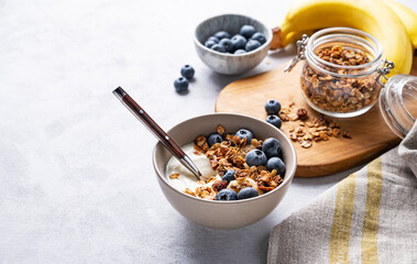 The concept of a healthy breakfast of yogurt, granola and fresh blueberry and banana on a light background. Homemade diet and protein food.