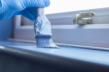 Person painting a window sill with blue paint using a brush. Do it yourself home improvement concept