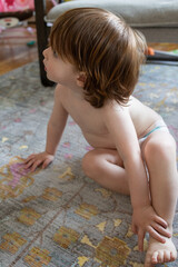 profile of sweet caucasian toddler boy with long hair wearing only a diaper on living room floor