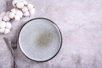 Obraz na płótnie Canvas Empty ceramic plate, cutlery and cotton branch on gray background top view