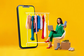 Happy stylish lady sitting near clothing rail in cellphone and using laptop, buying new shoe and...