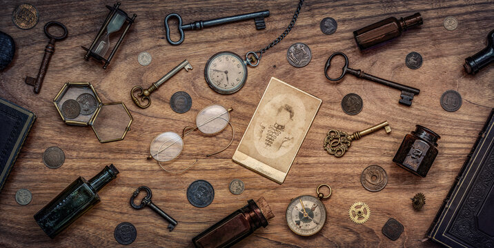 A collection of antique antiques is spread out on the table. Old coins, glasses, photography, glass bottles, keys, watch and compass. Vintage collection. History  background.