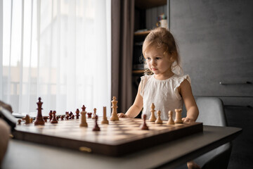 Father teaching his little daughter to play chess at the table in home kitchen. The concept early childhood development and education. Family leisure, communication and recreation.