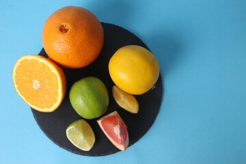 Citrus fruits, orange, lemon, grapefruit, lime lie on a black tray on a blue background with space for text and inventory. Healthy fruits. Vitamin C