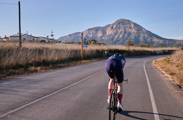 Fit cyclist on time trial aero bike riding his bike in aero position towards the mountains on empty...