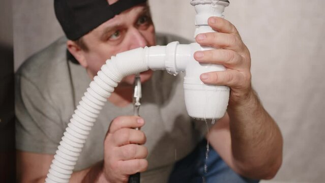 Plumber fixes water leak under sink. Water pours from siphon plumbing pipe.