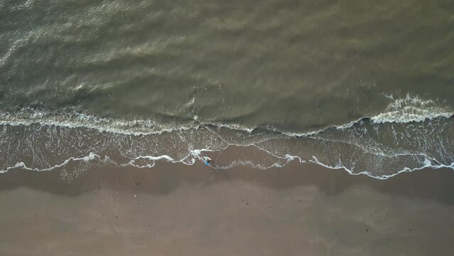 Young girl on sandy coast. Girl leaves footprints on sand. Attractive woman in blue sweater on beach. Girl walking along seashore. Aerial view of seashore. Beautiful ocean waves. Beach with  sand
