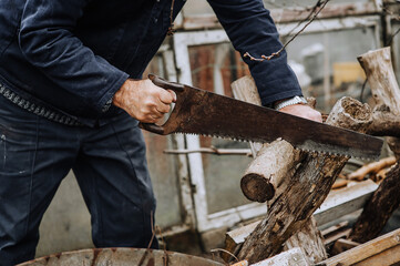 A man in a robe, a lumberjack, a worker saws a tree, a log with a hand saw, outdoors, in nature, at a sawmill. Photography, close-up, concept.