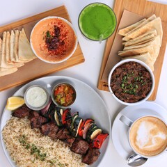 Flatlay spread of Mediterranean food on white table. Latte. Kabob. Pita bread.