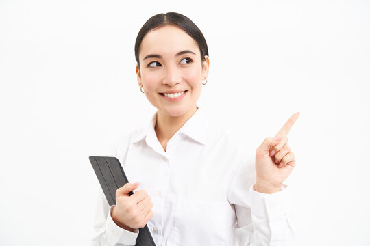 Image of young professional woman, pointing finger right, holding digital tablet, showing advertisement campaign, isolated on white background