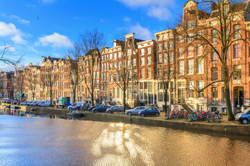 Cityscape on a sunny winter day - view of the houses and the city canal with boats in the historic center of Amsterdam, The Netherlands
