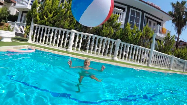 Play with a ball in the pool. A family have a funny time together with an inflatable ball in the home open air pool under summer sun.