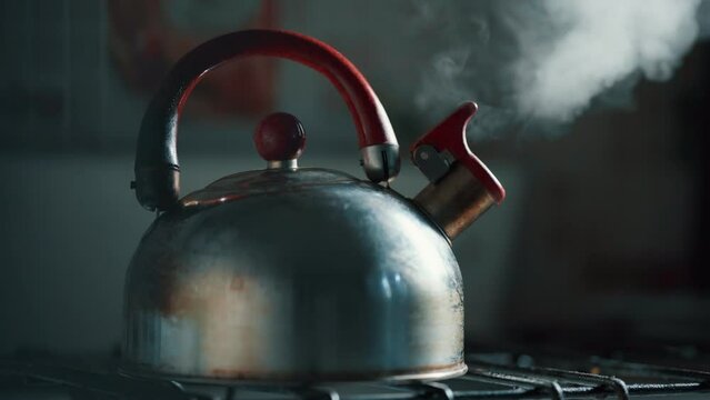 View of the steam from boiling water coming out of the spout of a metal kettle.
