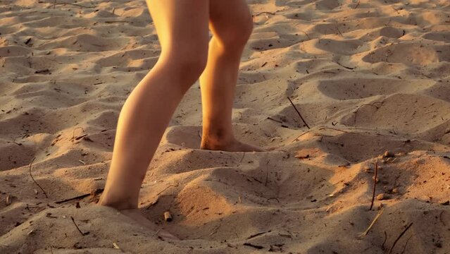 Legs of running, dancing, playing or jumping child on dry sand beach close-up. Active moving barefoot in sunset light. Summertime lifestyle. Vacation concept. Sea holiday. Happy childhood. Sport game.