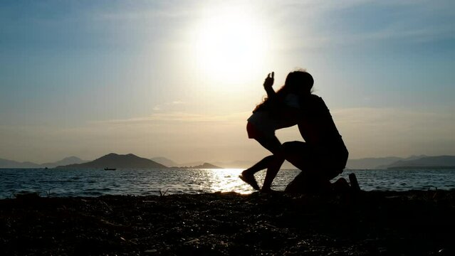 The father hugs the child. Silhouette of a happy dad hugging his daughter on the beach at sunset.