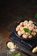 Sweets, peanuts in honey and sesame seeds in a ceramic bowl on a dark concrete background. Healthy sweets, handmade sweets.