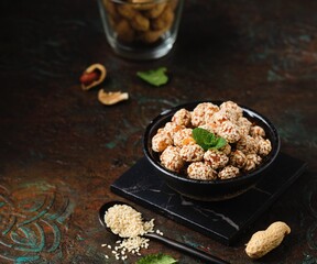 Sweets, peanuts in honey and sesame seeds in a ceramic bowl on a dark concrete background. Healthy sweets, handmade sweets.