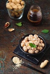 Sweets, peanuts in honey and sesame seeds in a ceramic bowl on a dark concrete background. Healthy sweets, handmade sweets.