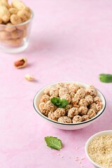 Sweets, peanuts in honey and sesame seeds in a white ceramic bowl on a pink concrete background. Useful sweets, handmade candies.